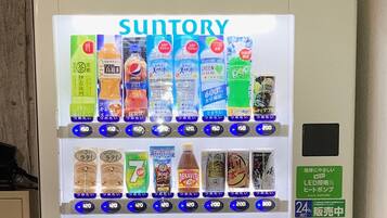 A vending machine with various beverages and snacks, including brands like Pepsi and 7UP, and a green sign indicating a 24-hour service.