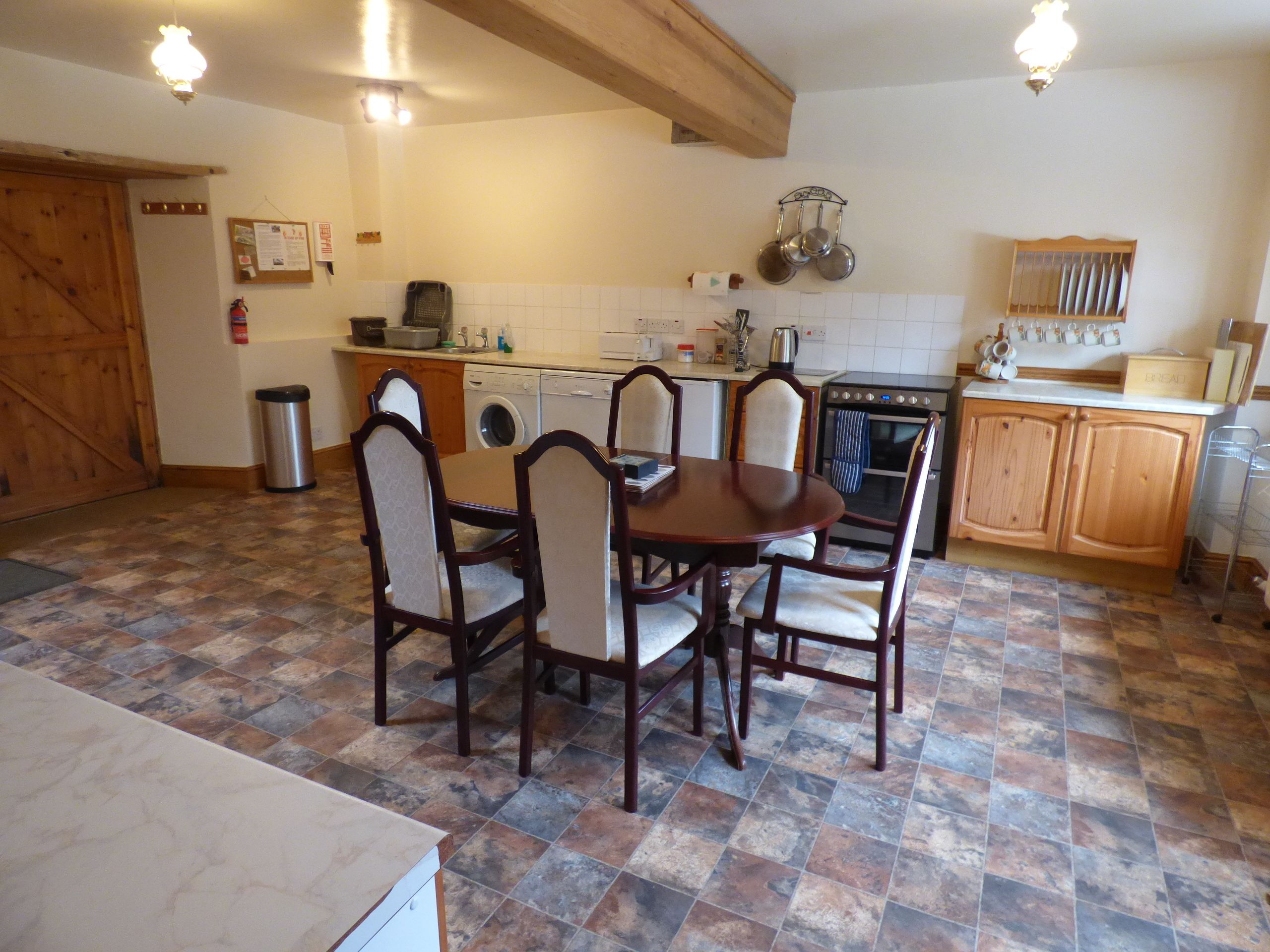 Una cocina con una mesa de comedor y sillas, lavadora, horno y un perchero para ollas.