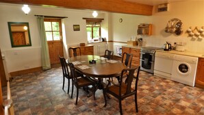 Een eethoek met een houten tafel en stoelen, een keuken met apparatuur, en een raam met gordijnen.
