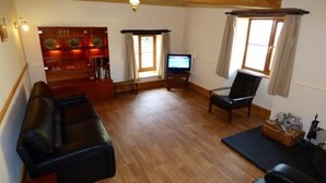 Een woonkamer met een houten vloer, een zwarte bank, een televisie en een stoel.