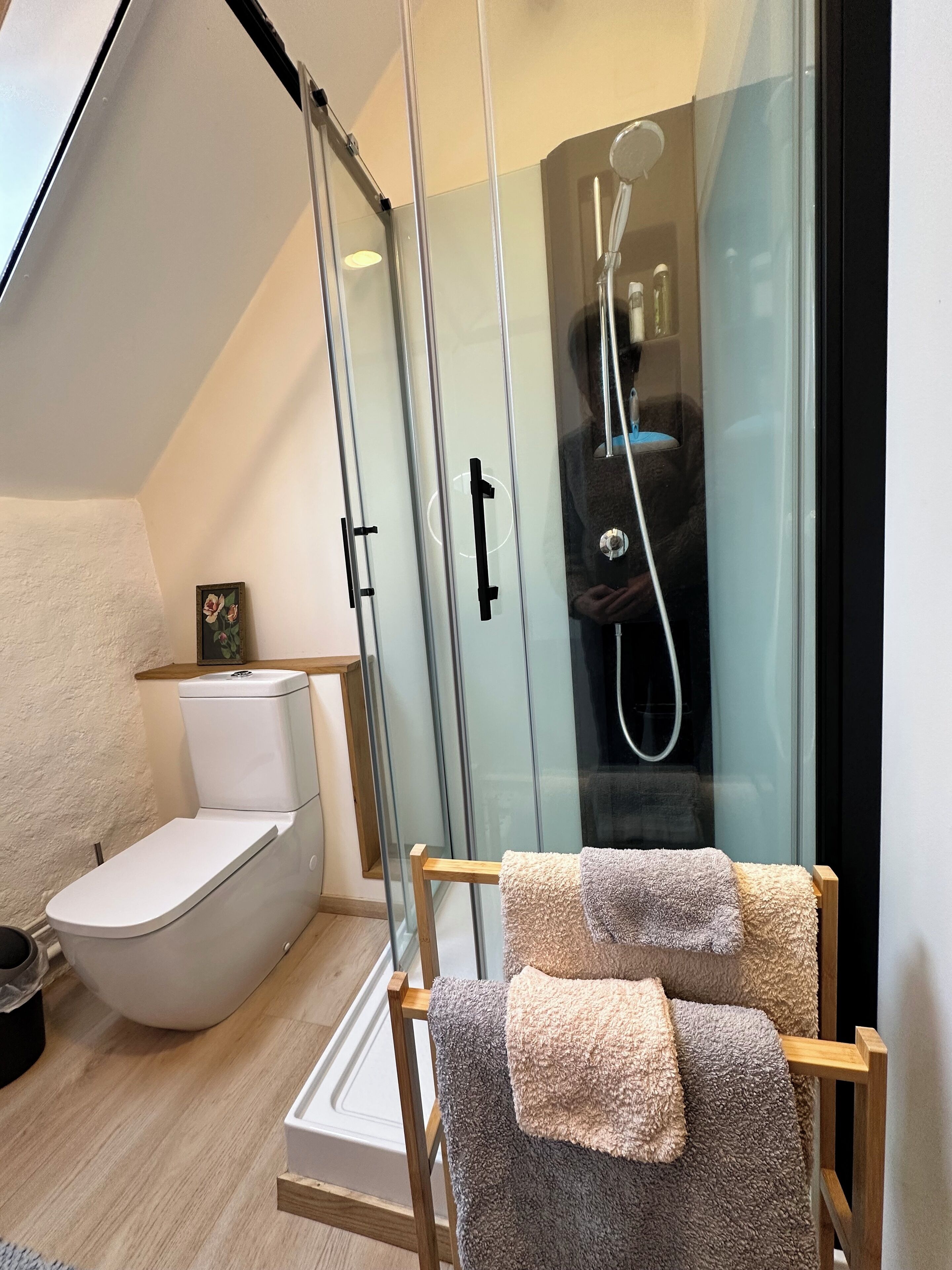 Une salle de bain moderne avec une douche à parois de verre, des toilettes et une chaise en bois sur laquelle sont posées des serviettes.