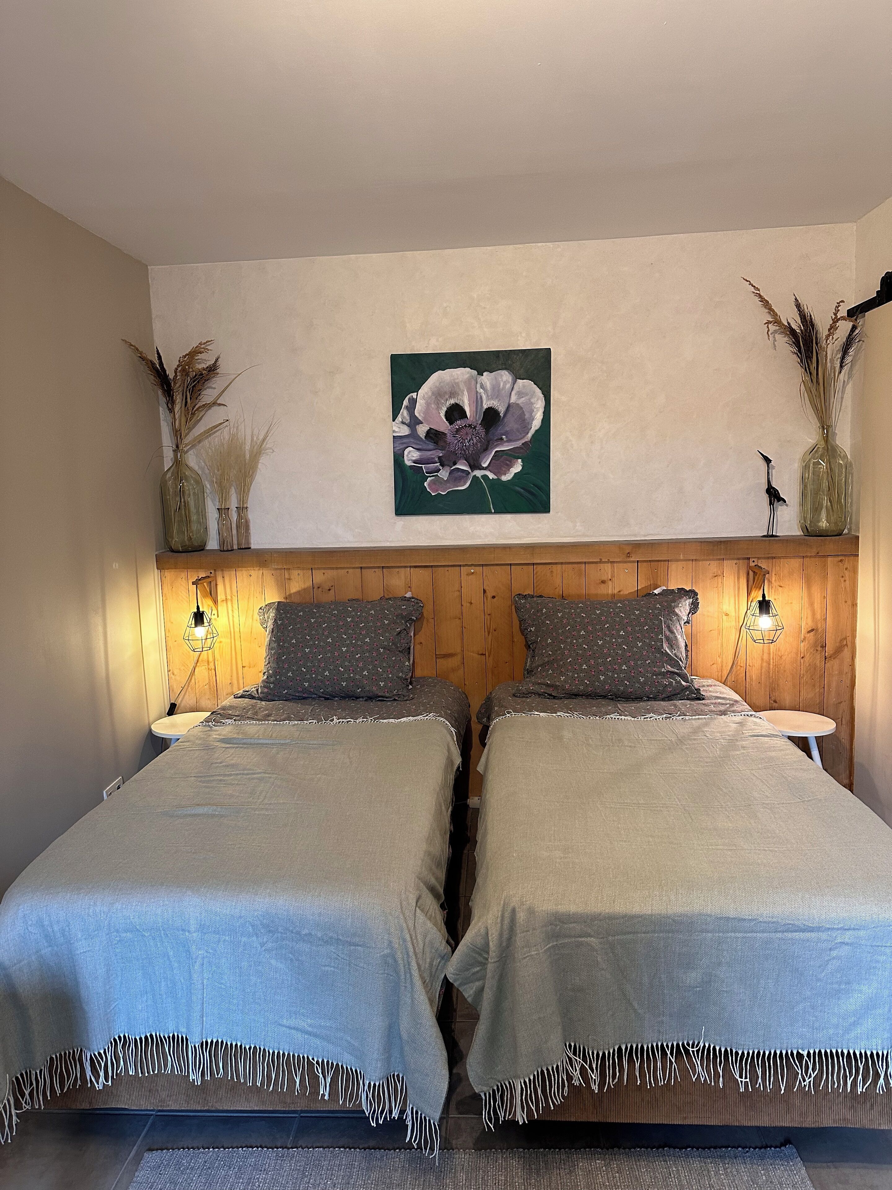 Una cama doble con cabecera de madera, dos mesitas de noche y un cuadro colgado en la pared con una flor.