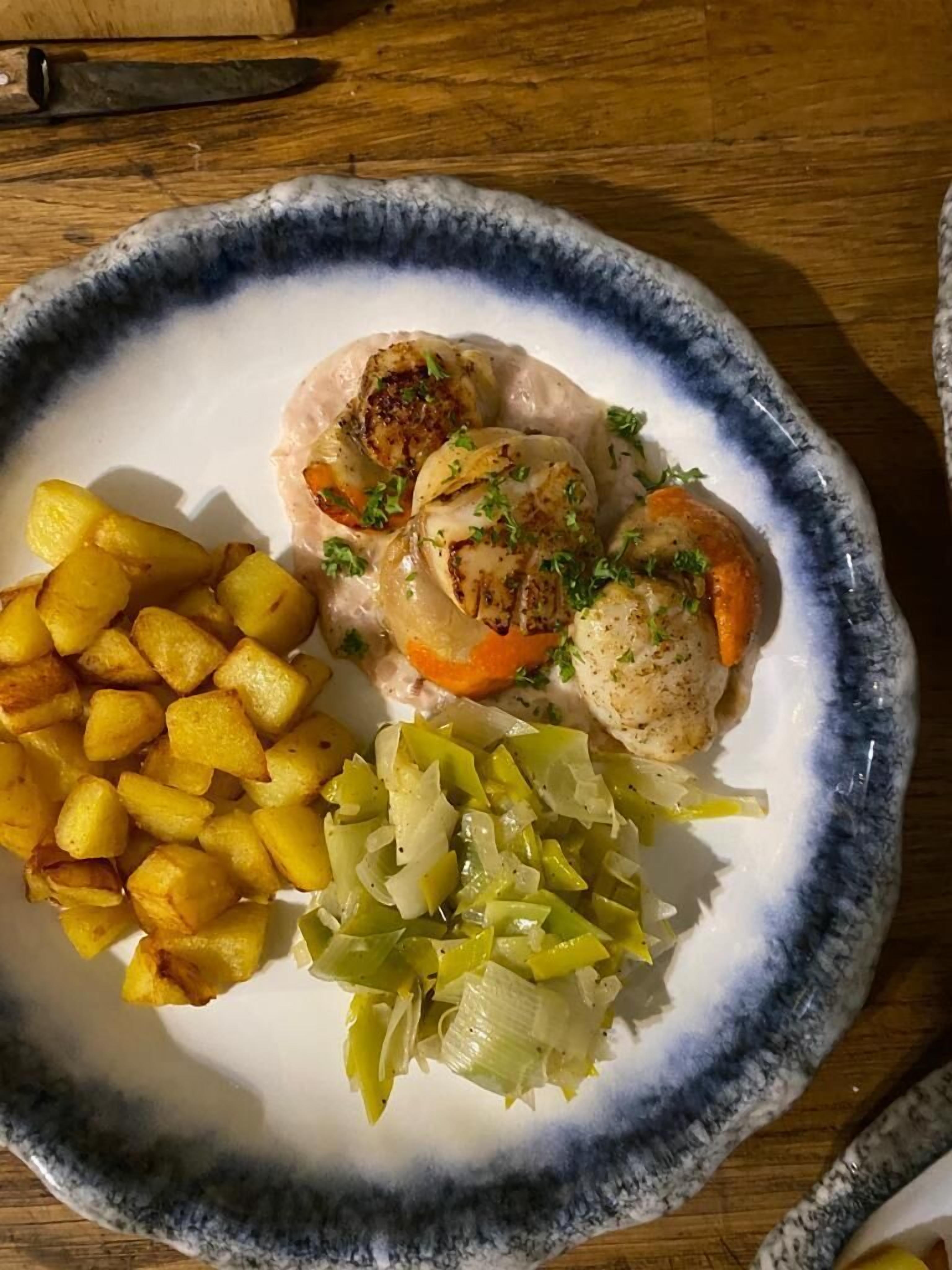 Une assiette de nourriture comprenant des noix de Saint-Jacques, des pommes de terre rôties et des légumes marinés.