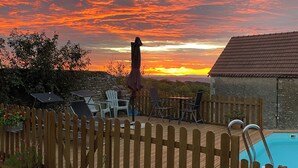 A wooden deck with outdoor furniture, a pool, and a sunset view. - B&B Maison Balady (Bellenaves)