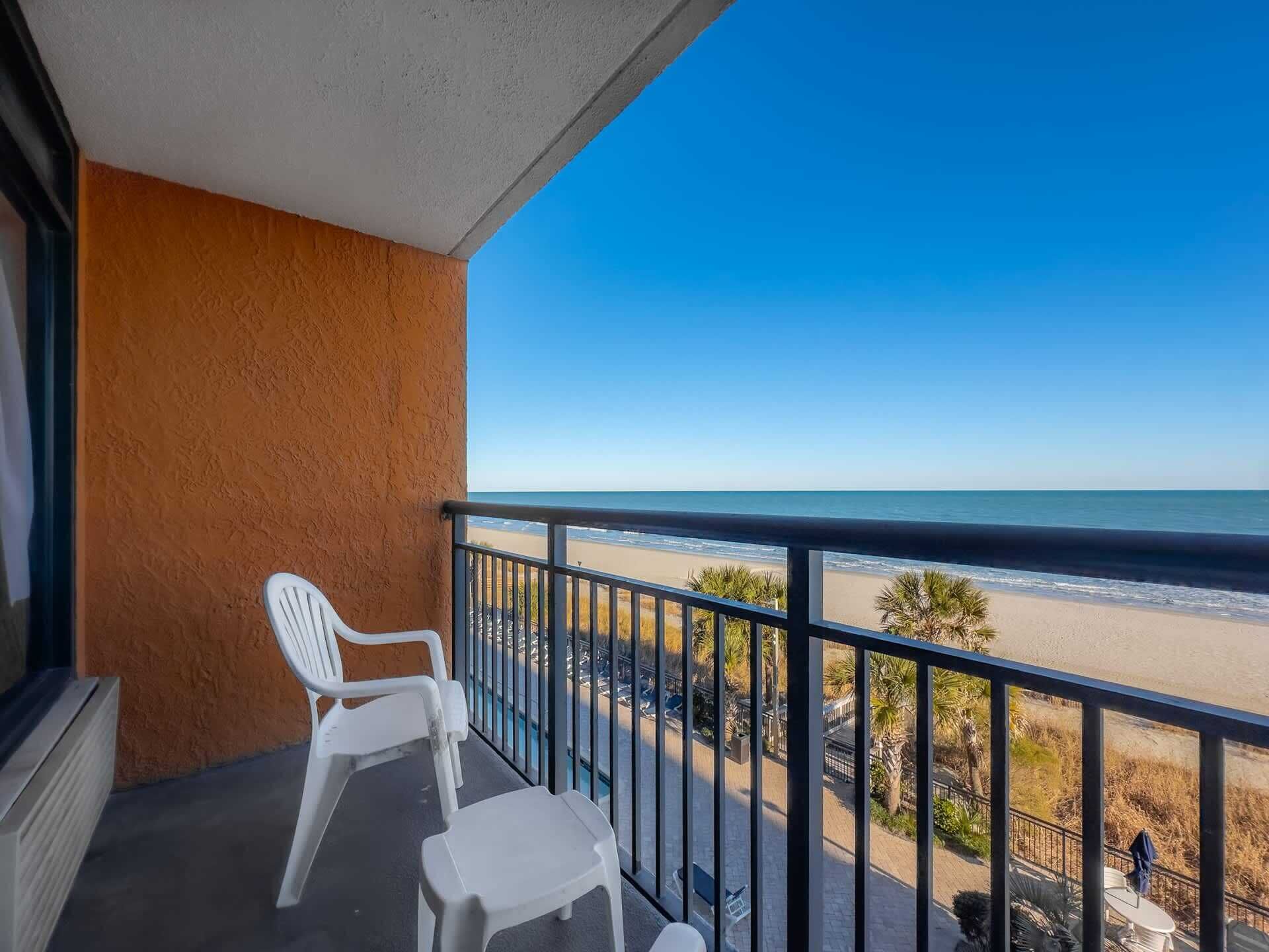 Ein Balkon mit Blick auf den Strand, ein weißer Stuhl und ein kleiner Tisch.
