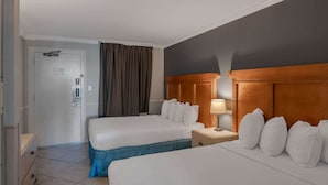 Ett hotellrum med två sängar, ett nattduksbord, en lampa, en dörr och ett fönster med gardiner.