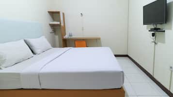 A hotel room with a bed, a desk, a chair, a TV, and a shelf with toiletries.