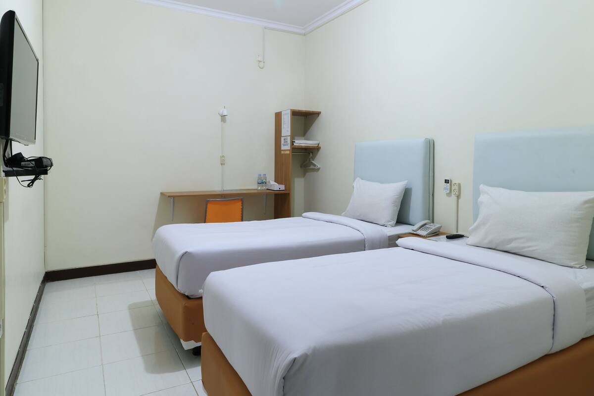 A hotel room with two beds, a desk, a chair, a TV, and a phone.