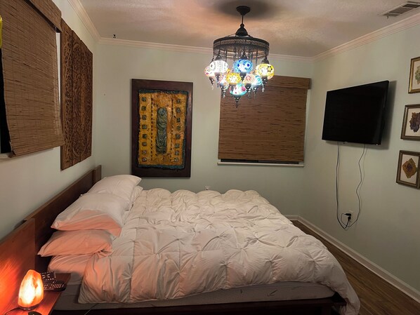 A bedroom with a bed, a wall-mounted TV, a decorative chandelier, and artwork on the walls. - The Luxury Lake Front Zen Casa (DeBary)