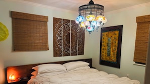 Une chambre à coucher avec un grand lit, un panneau décoratif au mur, un lustre et une œuvre d’art accrochée au mur.