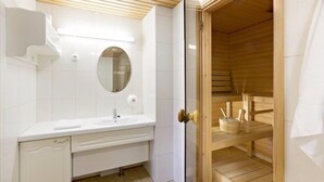 A modern bathroom with a white vanity, a mirror, and a wooden sauna.