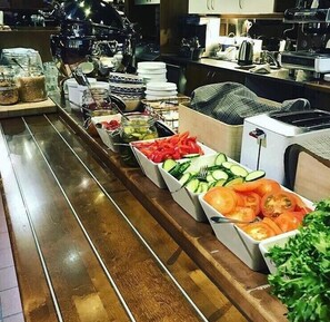 Un bufé con diversos alimentos, incluyendo pepinos en rodajas, tomates y vegetales encurtidos.