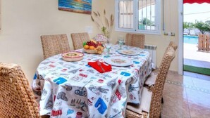 A dining area with a table set for four, wicker chairs, a painting on the wall, and a window with curtains.