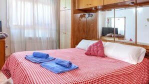 A neatly made bed with a checkered bedspread, a red pillow, and blue towels.