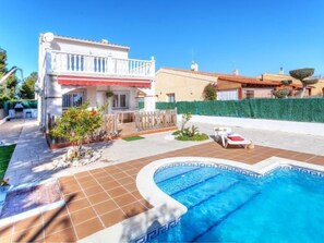 Uma casa de dois andares com piscina, varanda e jardim murado.