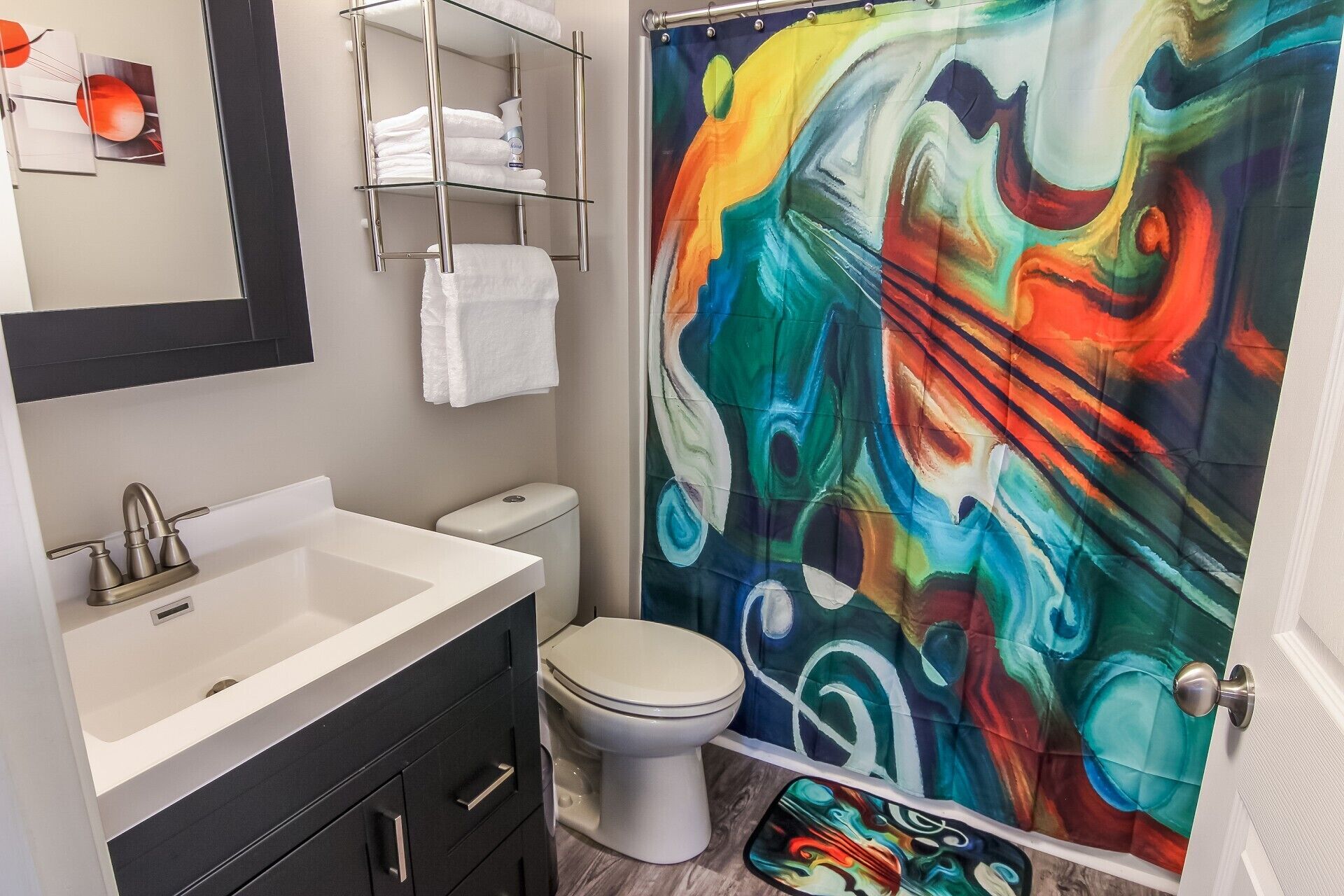 Un baño con un lavabo blanco, un inodoro y una cortina de ducha con un diseño abstracto y colorido.