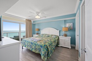 Une chambre à coucher comprenant un lit, deux tables de chevet, un ventilateur de plafond, une fenêtre avec vue et une porte.