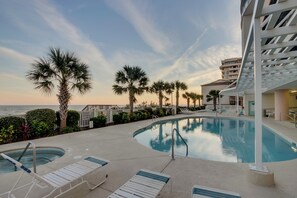 A pool area with lounge chairs, palm trees, and a view of the ocean. - Beautifully remodeled, oceanfront condo + Free Attraction Tickets! (North Myrtle Beach)