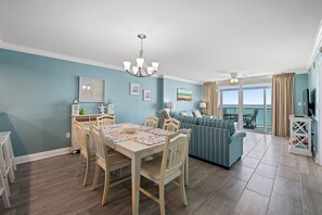A dining area with a table and chairs, a sofa, and a view of the ocean through large windows. - Beautifully remodeled, oceanfront condo + Free Attraction Tickets! (North Myrtle Beach)