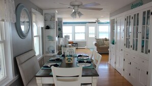 Een eethoek met een tafel voor vier personen, witte stoelen en uitzicht op de oceaan door grote ramen.