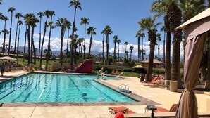 A swimming pool with clear blue water, surrounded by palm trees and lounge chairs. - Stunning elevated mountain and lake views at Palm Valley Country Club! (Palm Desert)