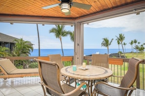 Enjoy ocean views from this outdoor seating area with a round table, chairs, and a ceiling fan.