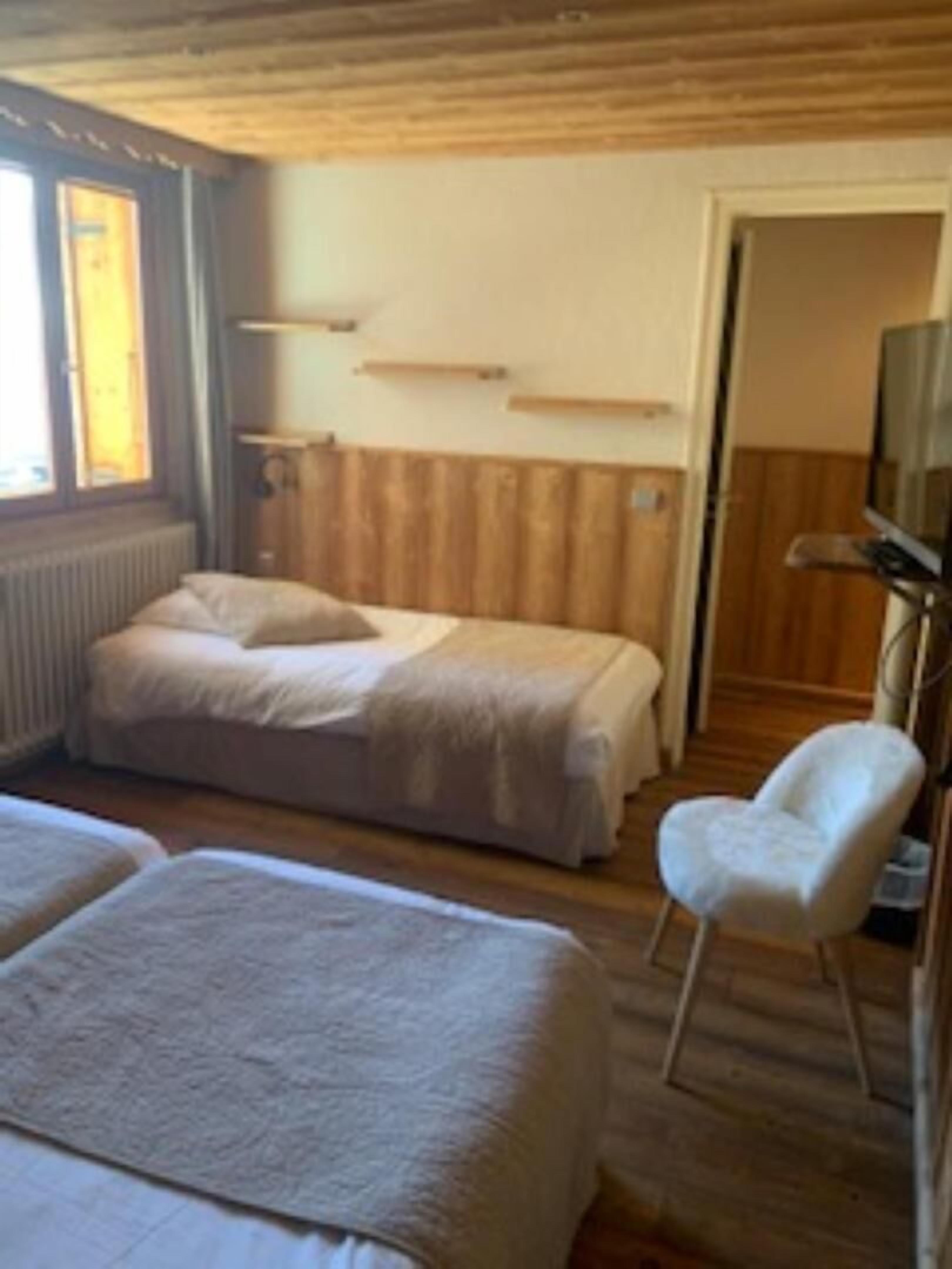 Quarto com duas camas, uma cadeira e uma televisão.
