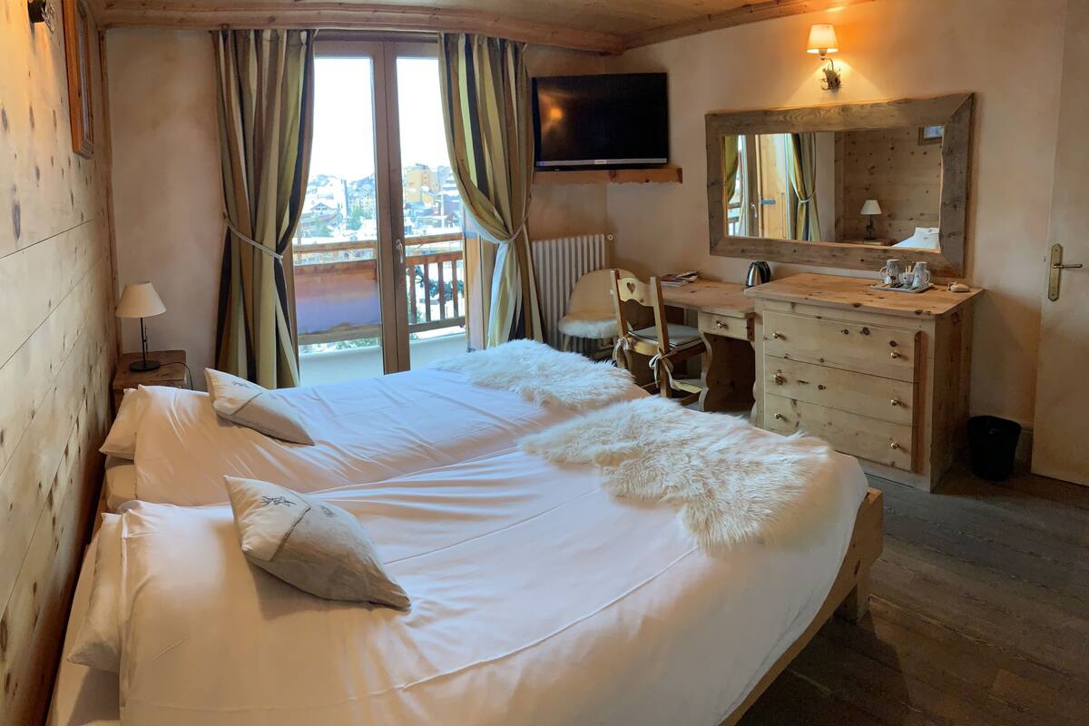 A hotel room with a large bed, a wooden dresser, a desk, a chair, a television, and a window with curtains.
