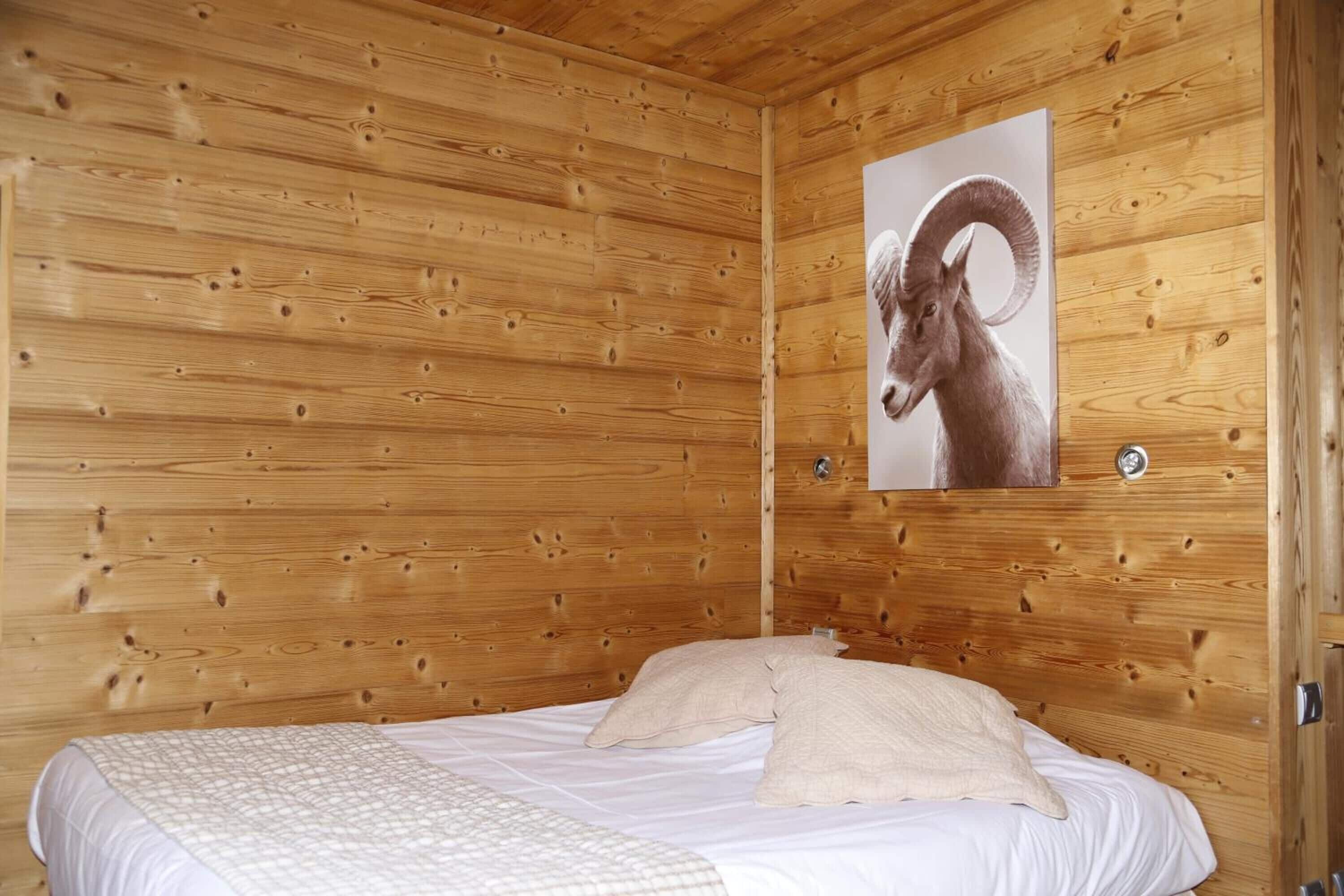 Une pièce de cabane en bois comprenant un lit, un tableau représentant un bélier accroché au mur et un mur en bois.