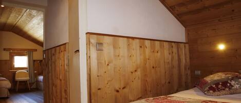 Quarto com painéis de madeira, uma cama, uma mesinha de cabeceira e uma janela.