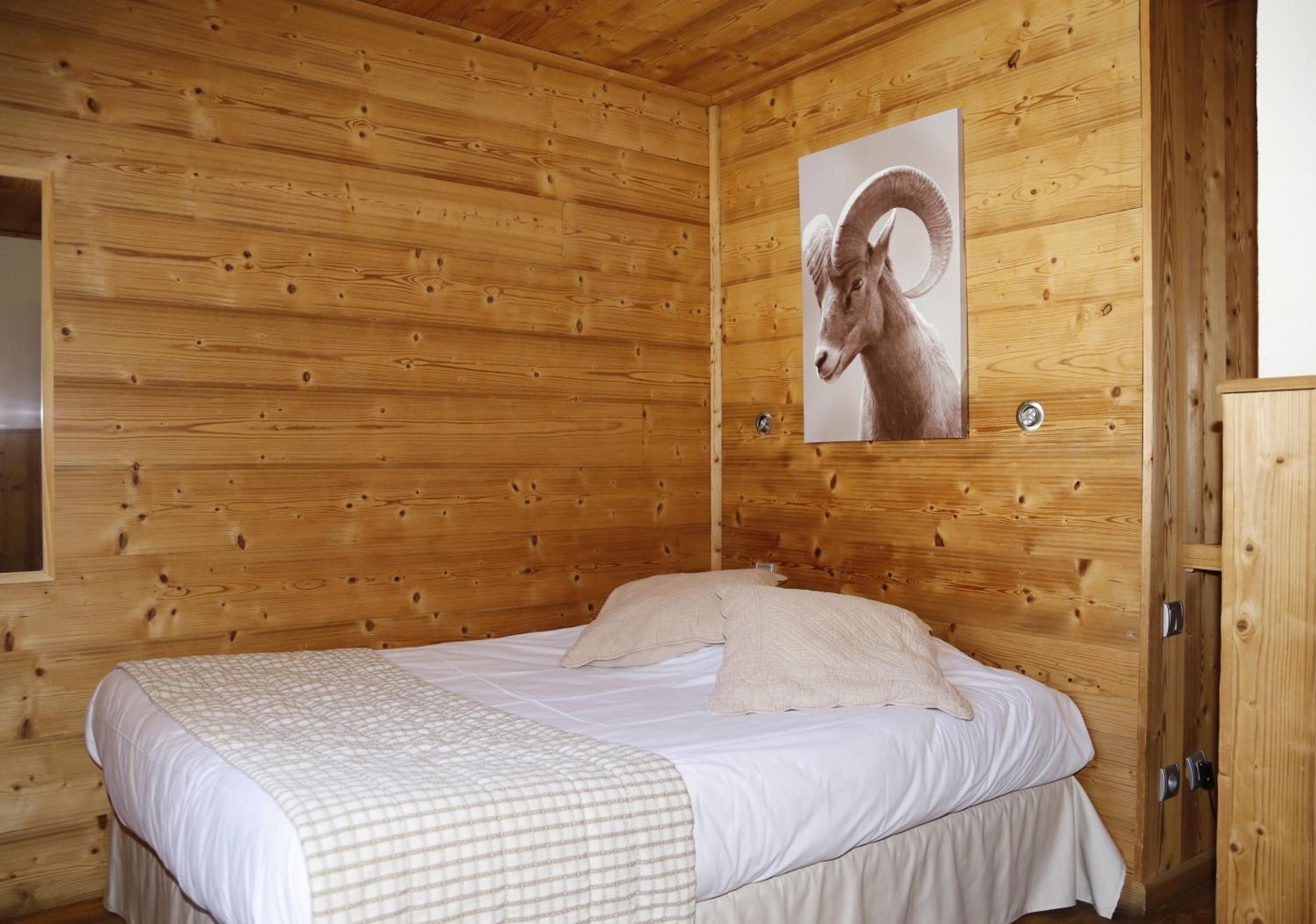 Una habitación tipo cabaña de madera con una cama, un cuadro colgado de un carnero y una ventana.
