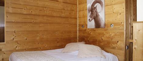 Een houten kamer met een bed, een aan de wand hangend schilderij van een ram, en een raam.