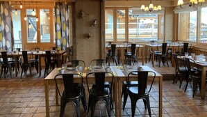 A restaurant with wooden interiors, large windows, and multiple tables with chairs. - Alp'Azur Hotel (Huez)