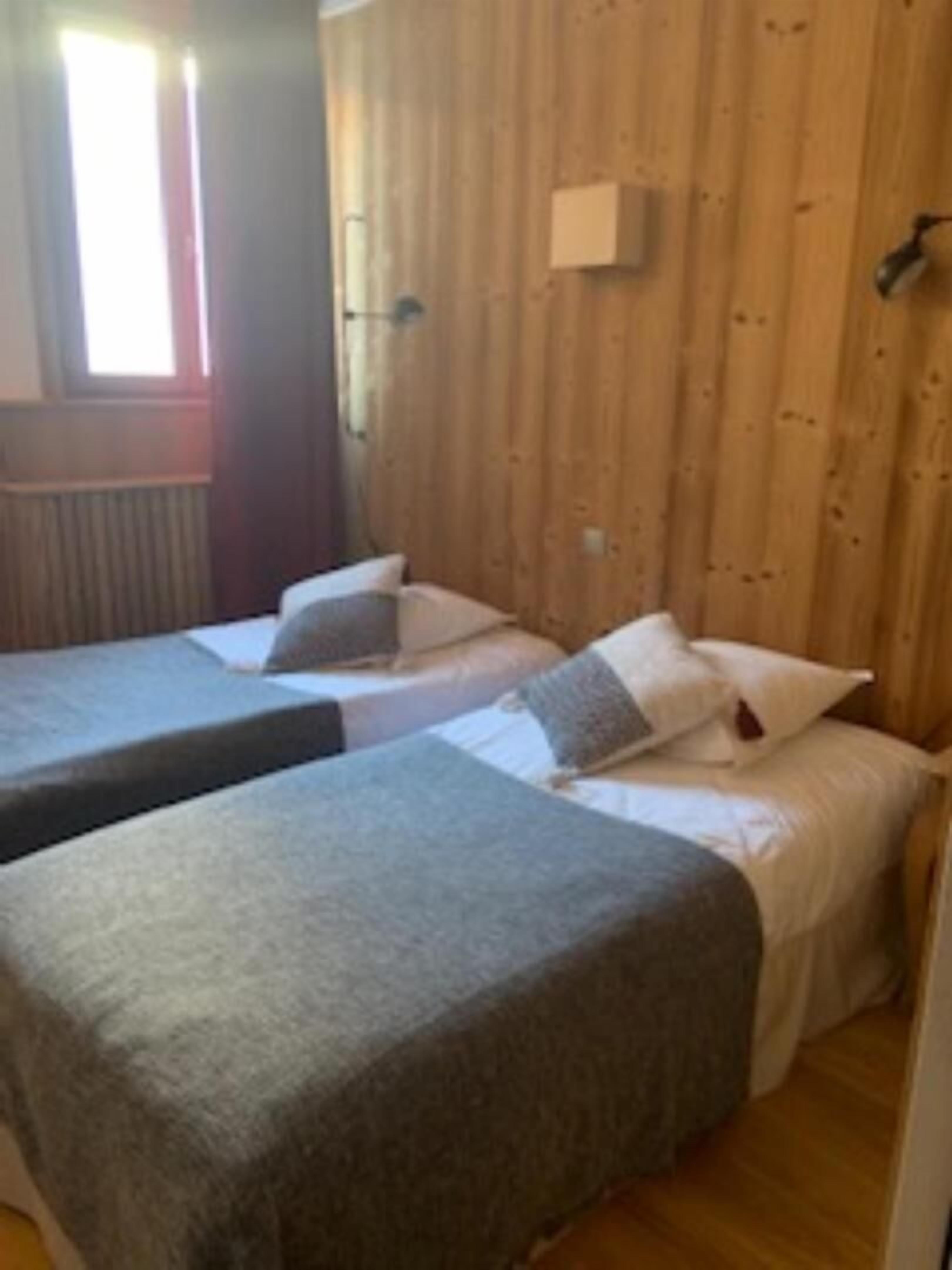Una habitación con dos camas, paredes de madera, una ventana y un radiador.