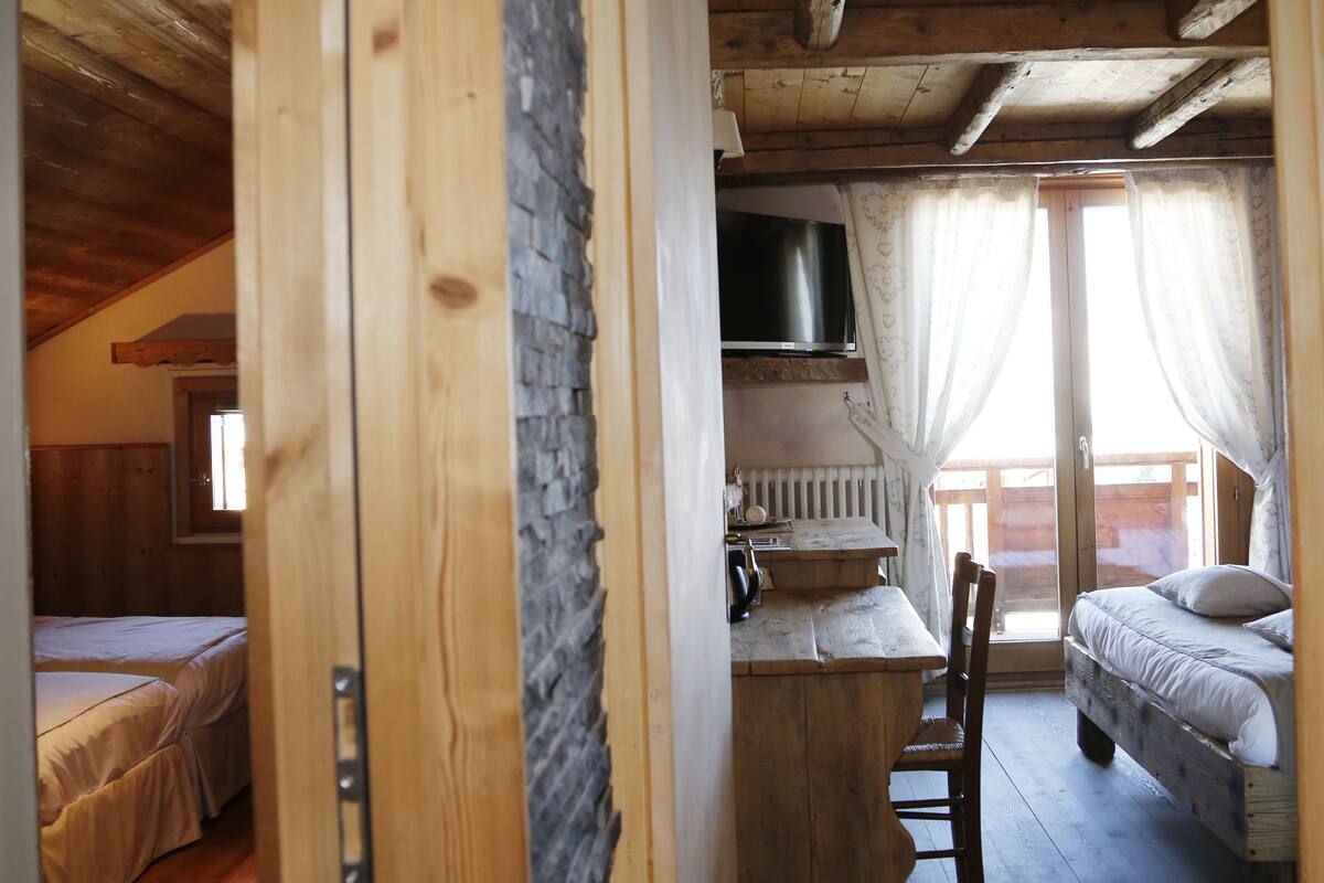 A cozy wooden cabin with a loft bedroom, a dining area with a stone wall, and a TV mounted above a fireplace.