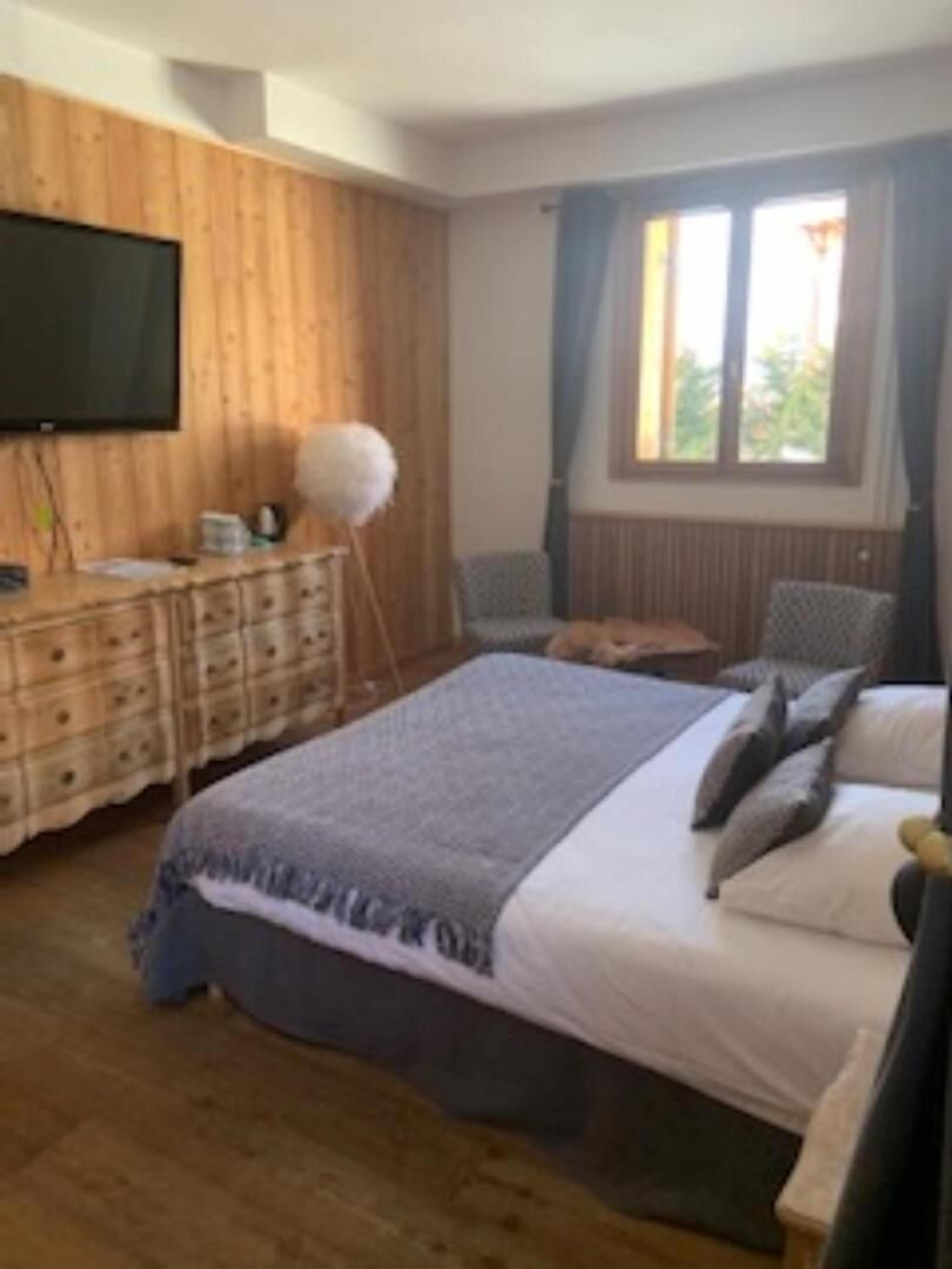 Una camera da letto con parete in legno, televisore a schermo piatto, comò, letto con cuscini e finestra con tende.