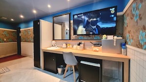 A hotel room with a large flat-screen TV mounted on the wall, a desk with a chair, a small trash bin, and a Samsung refrigerator. - Tirol Motel (Ulsan)