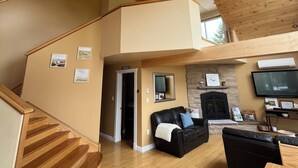 A spacious living area with a wooden staircase, a fireplace, a flat-screen TV, and a cozy seating area. - Luxury House in the Cavendish Area with Pool, Hot Tub and Air Conditioning (Stanley Bridge)