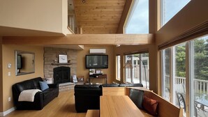 A spacious living area with a high ceiling, wooden flooring, and large windows offering a view of the outdoors. - Luxury House in the Cavendish Area with Pool, Hot Tub and Air Conditioning (Stanley Bridge)