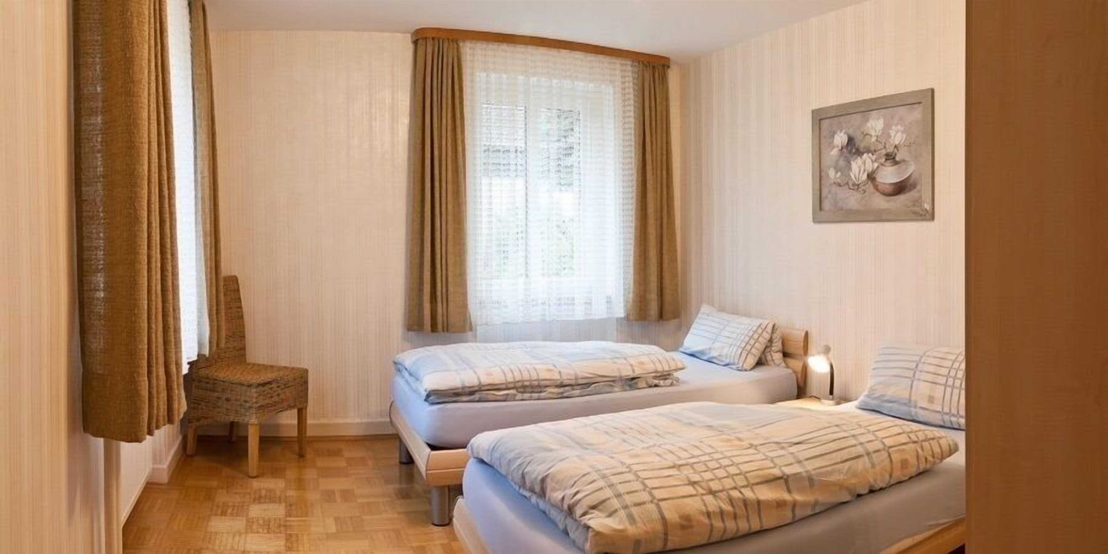 Ein Schlafzimmer mit zwei Betten, einem Sessel, einem Fenster mit Vorhängen und einem Gemälde an der Wand.