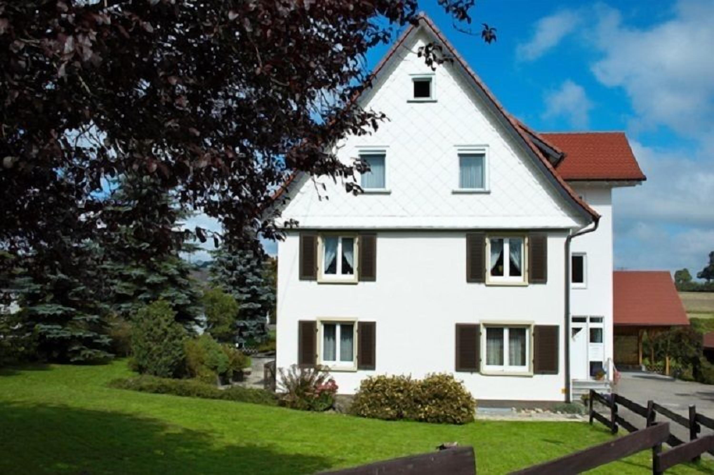 Een wit huis met twee verdiepingen en een rood dak, omgeven door een groen gazon en bomen.