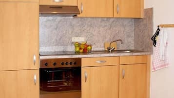 A kitchen with wooden cabinets, a stainless steel oven, a marble countertop, and a sink.