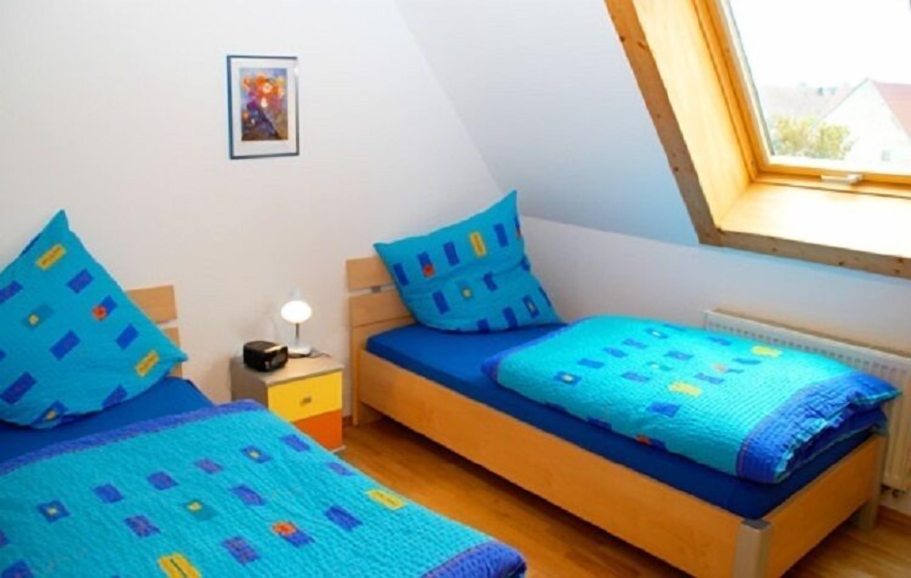A bedroom with two beds, a nightstand, a lamp, and a window with a view of the outside.