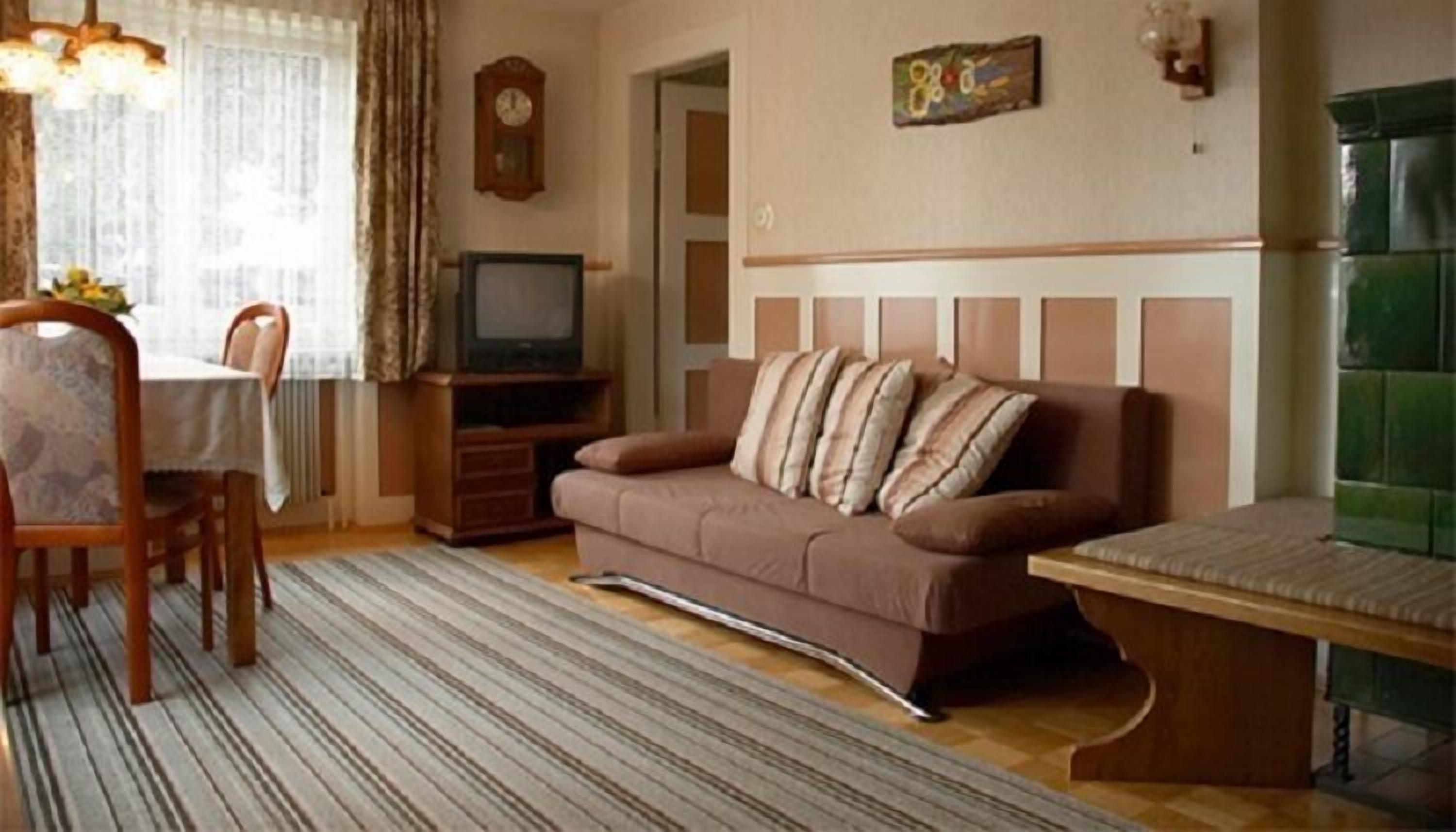 Ein Wohnzimmer mit einer Couch, einem Fernseher, einem Esstisch mit Stühlen und einem gemusterten Teppich.