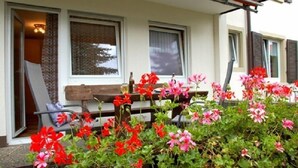 Une maison avec un porche, un banc et une table décorée de fleurs.