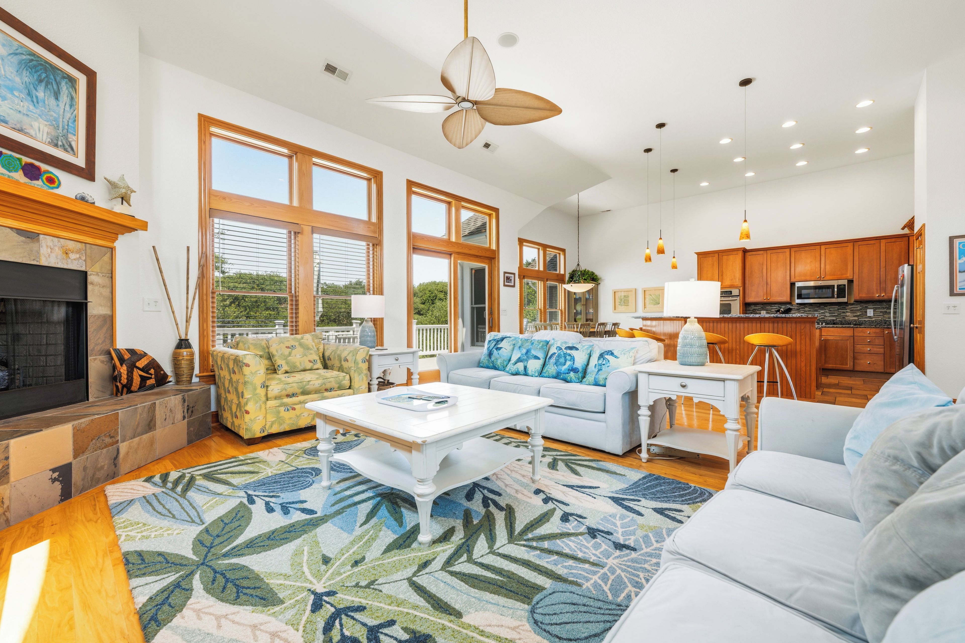 A spacious living room with a fireplace, large windows, and a kitchen area.