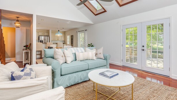 A spacious living room with a light blue sofa, white armchairs, and a round coffee table. A ceiling fan and skylight are visible above. - Charleston-area 3BR, Close to Beach or Downtown, Walk to Shem Creek (Mt Pleasant)