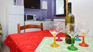 A dining table with a red tablecloth and colorful wine glasses, a bottle of wine, and a microwave in the background. - Bacvice Beach Apartment (Split)