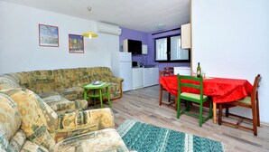 A living room with a sofa, a dining table with chairs, a kitchen area, and a window with curtains. - Bacvice Beach Apartment (Split)