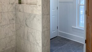 A bathroom with white subway tiles, a shower area with marble walls, and a door leading to another room. - Walk to Journeyman Renovated Spacious Victorian House, Beautiful Vintage Details (Three Oaks)